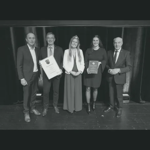 Fünf Personen auf einer Bühne mit Urkunde und Plakette bei einer Weinprämierung